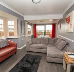 A living room with a brown leather sofa grey sectional sofa black rug and dining table with red curtains at Swiss Cottage in Wilsthorpe near Bridlington