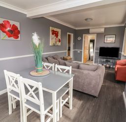 A dining area with a table and chairs next to a living room with sofas a television and wall art at Swiss Cottage Wilsthorpe near Bridlington