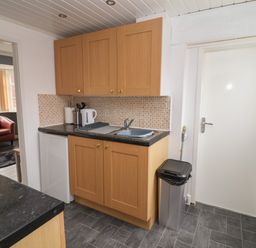 A kitchen with wooden cabinets a sink a kettle utensils and a trash bin at Swiss Cottage in Wilsthorpe near Bridlington
