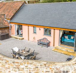An outdoor seating area with a table and chairs and a bench outside a building with open doors at The Farm Office in Bampton Devon