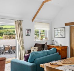 A living room with a blue sofa brown armchair wooden sideboard dining table with bread and outdoor seating area at The Farm Office in Bampton Devon