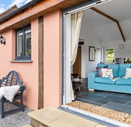 An open doorway showing a blue sofa with cushions inside and a black bench with a white throw outside at The Farm Office in Bampton Devon