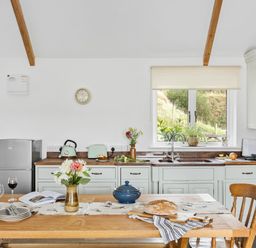 A kitchen with wooden table set with bread and flowers a window and appliances at The Farm Office in Bampton Devon