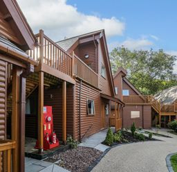 An outdoor view of wooden lodges with balconies and paved pathways surrounded by plants at Classic Lodge 30 in Dyserth