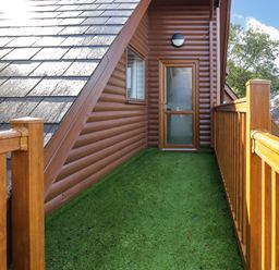 A balcony with green artificial grass flooring wooden railing and a glass door at Classic Lodge 30 in Dyserth