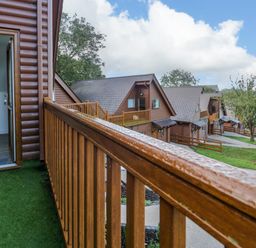 A balcony with wooden railing overlooking a row of brown wooden lodges and a pathway at Classic Lodge 30 in Dyserth