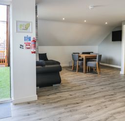 A room with a wooden dining table and four chairs a black sofa a wall-mounted tv and a door leading outside at Classic Lodge 30 in Dyserth