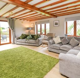 A living room with two grey sofas a green rug wood beam ceiling and large windows at Pondarosa in Newbridge-On-Wye