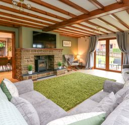 A living room with a stone fireplace a large television two gray sofas a green rug and wooden ceiling beams at Pondarosa in Newbridge-On-Wye