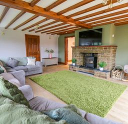 A living room with a green rug a stone fireplace a TV on the wall and grey sofas at Pondarosa in Newbridge-On-Wye