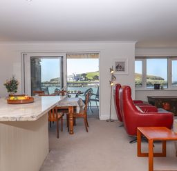A living and dining area with red leather chairs a wooden table and a granite countertop with a sea view at 14 Burgh Island Causeway in Bigbury-On-Sea