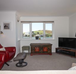 A living room with a red armchair gray footstool antique chest and television at 14 Burgh Island Causeway in Bigbury-On-Sea