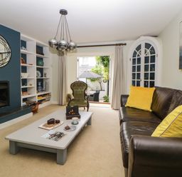 A living room with a brown leather sofa with yellow cushions a green armchair a coffee table a fireplace and built in shelves at Lower Culvermead in Chaddlehanger near Tavistock