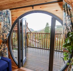 A wooden room with a circular glass door opening onto a balcony with wooden railings at The Kites Nest in Pont-rhyd-y-groes near Pontrhydfendigaid Snowdonia