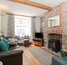 A living room with a leather sofa pillows a stone fireplace and a television at Teal House in Lyme Regis