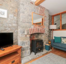 A living room with a stone fireplace a wood stove a blue sofa and a television on a wooden stand at Teal House in Lyme Regis