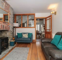 A living room with a stone fireplace a black stove two sofas with cushions and a wooden floor at Teal House in Lyme Regis