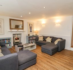 A living room with two gray sofas a coffee table a wood stove a large mirror and lobster artwork at Tan y Craig in Solva