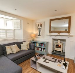 A living room with a sofa a coffee table with dominoes and wine a fireplace and bookshelves at Tan y Craig in Solva