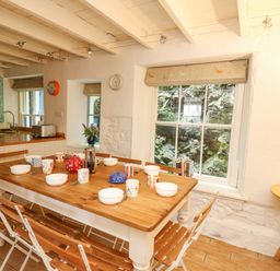 A dining room with a wooden table and chairs set with bowls mugs and teapots next to windows at Tan y Craig in Solva