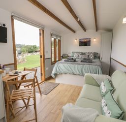 A bedroom with a bed green sofa wooden table and chairs open door showing outside at Tan Y Castell Shepherds Hut in Llangollen