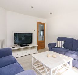 A living room with two blue sofas a white coffee table and a television on a white stand at 1 Camperdown Lodge in Salcombe