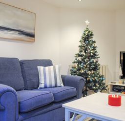 A living room with a blue sofa a Christmas tree and a white coffee table with a red candle at 1 Camperdown Lodge in Salcombe