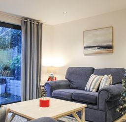 A living room with a sofa two striped pillows a coffee table with a red candle painting on the wall and a decorated Christmas tree at 1 Camperdown Lodge in Salcombe