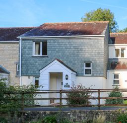 A two-story house with grey slate siding and a porch behind a wooden fence at Primrose Cottage in Goldenbank near Falmouth