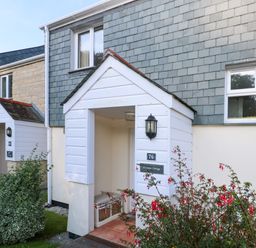 The entrance of a house with white porch and tiled floor with red flowers in the front at Primrose Cottage Goldenbank near Falmouth