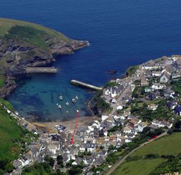An aerial view of a coastal village with houses boats in a small harbor and green hills at St Samson in Port Isaac