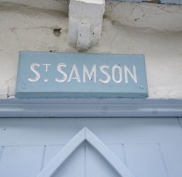 A blue sign with white text reading St Samson mounted above a light blue door at St Samson in Port Isaac