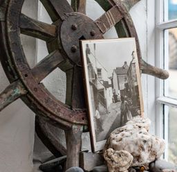 A ship wheel with an old black and white photograph and stones on a windowsill at St Samson Port Isaac