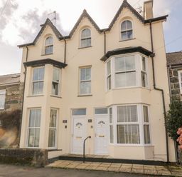 The exterior of a beige semi detached house with two white front doors and three peaked roof sections at Bay View in Criccieth