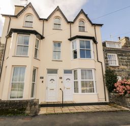 Two attached cream colored houses with white doors and bay windows at Bay View in Criccieth