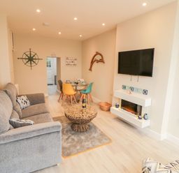 A living room with a gray sofa a round coffee table a wall-mounted tv a dining table with colorful chairs and decorations at Bay View in Criccieth