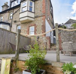 An outdoor patio with chairs and a rope railing beside a stone house at Coastal View in Lyme Regis