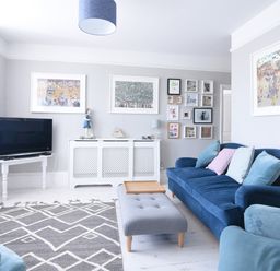 A living room with blue sofas grey ottoman and a television at Coastal View in Lyme Regis