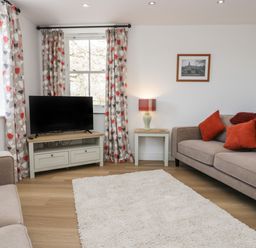 A living room with two sofas a television on a stand a side table with a lamp and patterned curtains at Dalegarth Hall Farm Cottage 1 Boot near Eskdale Green