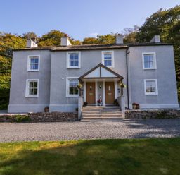 A two-story gray house with two front doors and a small porch area surrounded by trees at Dalegarth Hall Farm Cottage 1 Boot near Eskdale Green