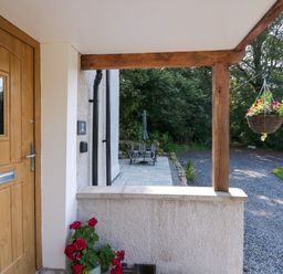 A wooden front door with flowers in a pot and a hanging flower basket on a porch at Dalegarth Hall Farm Cottage 1 Boot near Eskdale Green