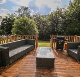 An outdoor wooden deck with rattan sofa chairs a glass top coffee table and a barbecue grill at Gelli Barn Near Llandeilo