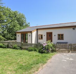 A small house with wooden doors and windows and a fenced garden with grass and plants at Adipit Stables Buckland Brewer near Bideford