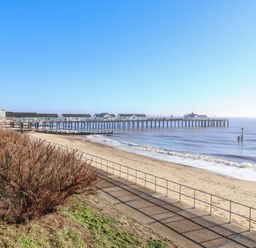 A sandy beach with a pier extending into the sea and a pathway with a railing alongside the beach at Pebbles in Southwold