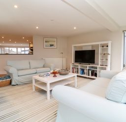 A living room with two sofas a white coffee table a striped rug and a TV unit at Pebbles in Southwold