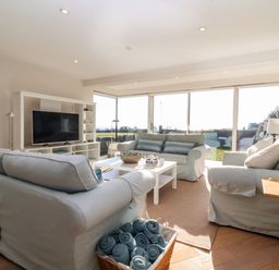 A living room with sofas a coffee table a television and large windows overlooking a garden at Pebbles in Southwold