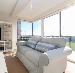 A living room with a white sofa and striped cushions facing a wall unit with a television and shelves at Pebbles in Southwold