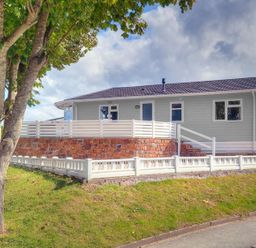 A house with a white fence on a grassy slope and a tree in front at E19 The Warren in Abersoch