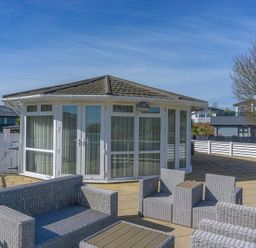 An outdoor patio area with wicker seating and a circular building with large windows at E19 The Warren in Abersoch