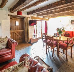 A living room with wooden beams a wooden door a dining table with chairs and red sofas at Ty Fferm Hen in Talybont-on-Usk